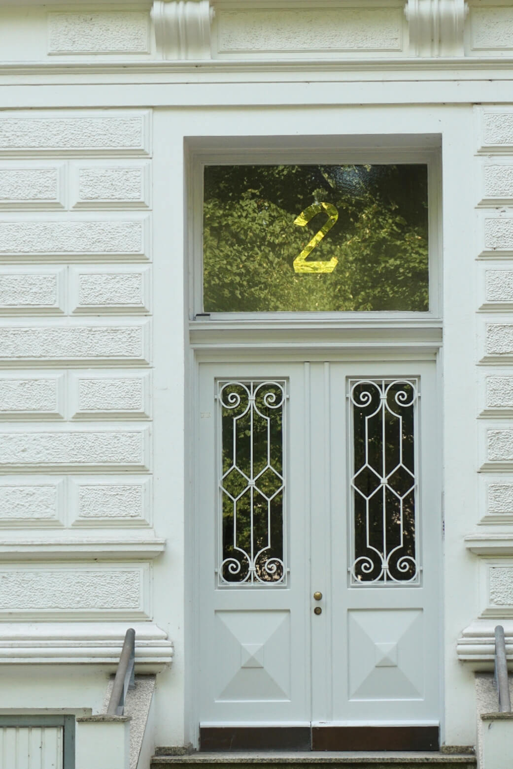 Weiß gestaltete Altbau-Eingangstür des Instituts mit verzierten Fenstergittern und goldener Hausnummer 2 im Oberlicht.